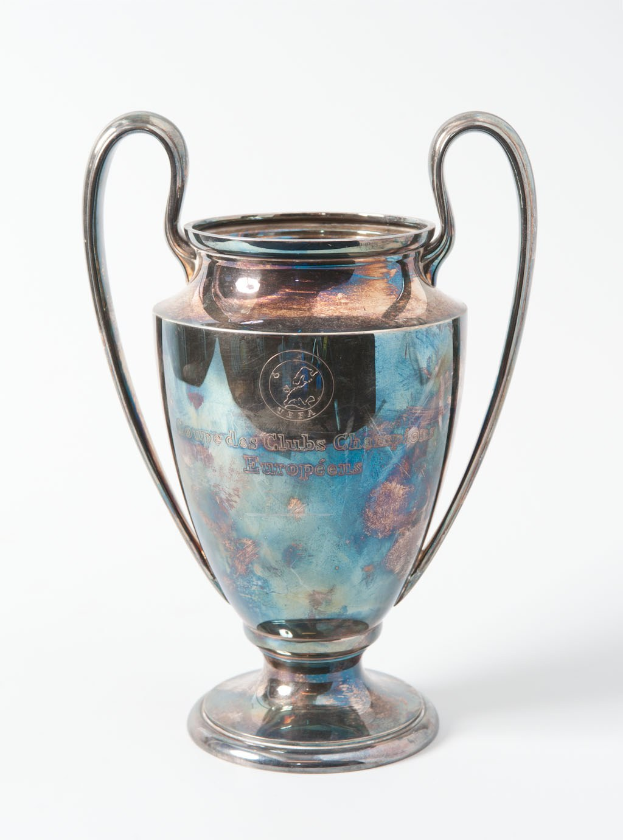 Der UEFA Champions League-Pokal, ein stählerner Becher mit zwei Griffen und einem blauen und silbernen Farbschema, der mit 'UEFA Champions League' beschriftet ist, vor einem weißen Hintergrund.