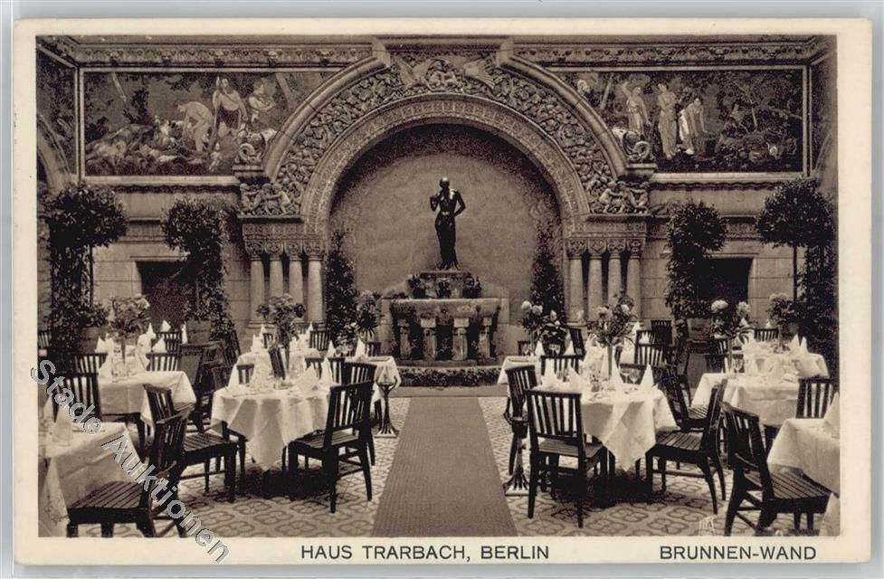 Schwarze und weiße Aufnahme eines alten Berliner Restaurant-Interieurs mit Tischen, Stühlen, Blumenvasen, einer Statue, Wandskulpturen, Pflanzen und Text unten.