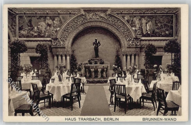 Schwarze und weiße Aufnahme eines alten Berliner Restaurant-Interieurs mit Tischen, Stühlen, Blumenvasen, einer Statue, Wandskulpturen, Pflanzen und Text unten.