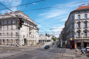 Eine Stadtstraße mit Autos, Fußgängern, Gebäuden, Strommasten, Ampeln, Schildern, Bäumen und einer bewölkten Himmel.