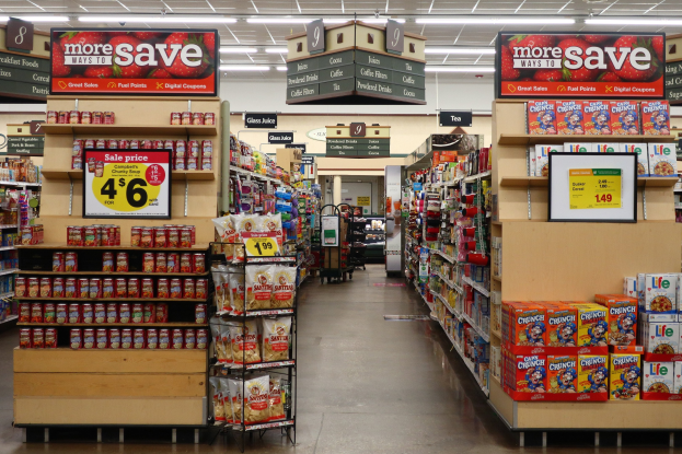 Ein Kiosk-Innenraum mit verschiedenen Lebensmitteln auf Regalen, Regalen und dem Boden, Deckenleuchten und Informationsschildern.
