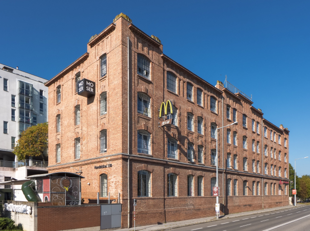 Ein großes Backsteingebäude von McDonald's an einer Straßenecke in Berlin, Deutschland, mit umgebender Straßeninfrastruktur und Fahrzeugen.