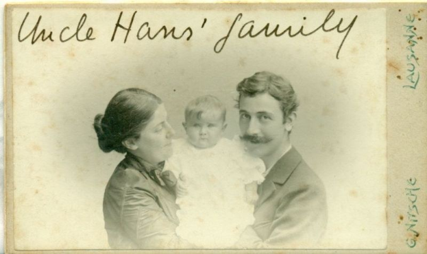 Ein altes Foto eines Mannes im Anzug und Krawatte, einer Frau mit einem Baby auf dem Arm, mit der Aufschrift "Onkel Hans' Familie" oben, alle strahlend.