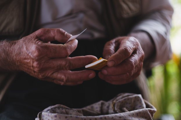 Alter Mann mit einem Blatt Papier in der Hand, der besorgt wirkt und vor einem unscharfen Hintergrund zu sehen ist.