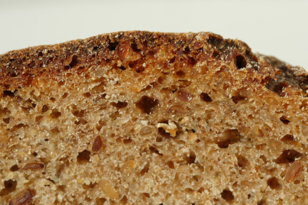 Nahaufnahme eines goldbraunen Roggenbrotlaibs mit leicht knuspriger Kruste und weichem Inneren, mit Rosinen bedeckt auf einem weißen Teller.