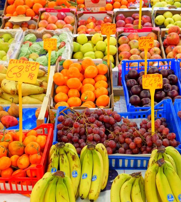 Ein Marktstand mit verschiedenen Obst- und Gemüsesorten und daran befestigten Preisschildern.