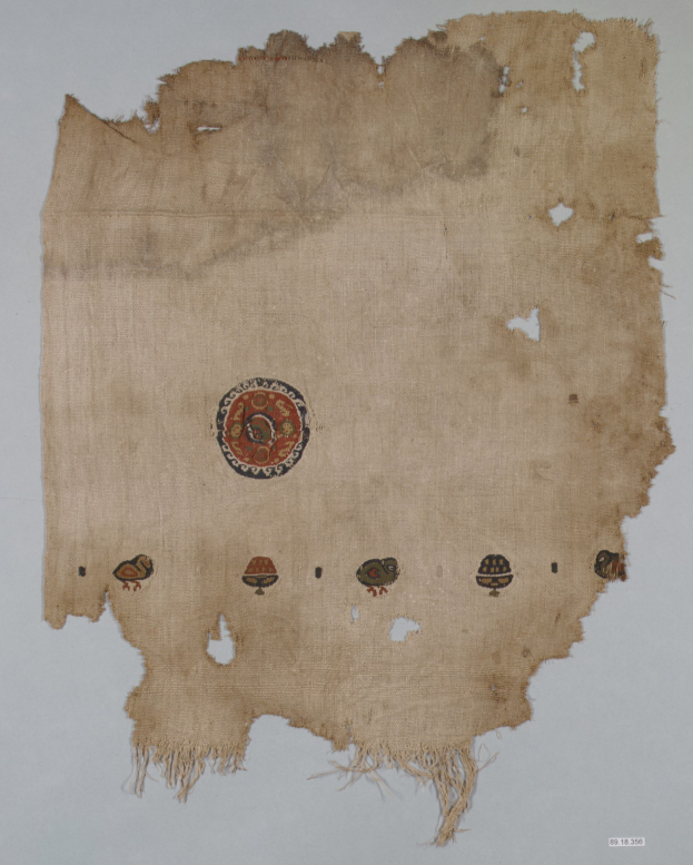 Ein Stück Stoff mit einem leuchtenden, detailreichen kreisförmigen Design, bestehend aus verschiedenen Formen und Farben, einschließlich Kreisen, Quadraten und Dreiecken, vor einem weißen Hintergrund.