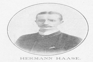 Schwarz-weiß-Porträt des deutschen Komponisten und Pianisten Hermann Haase in einem Anzug mit Schnurrbart und ernstem Gesichtsausdruck, mit deutschem Text unten.