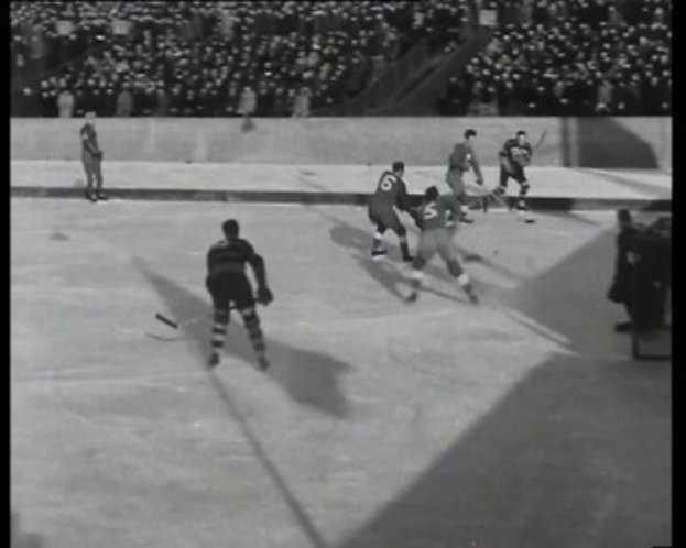 Schwarzes und weißes Foto von Männern, die Hockey auf einem Eisplatz spielen, mit Zuschauern in den Tribünen.