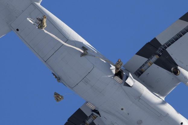 Ein großes weißes Flugzeug mit uniformierten Personen auf der Seite, das durch einen hellblauen Himmel fliegt.