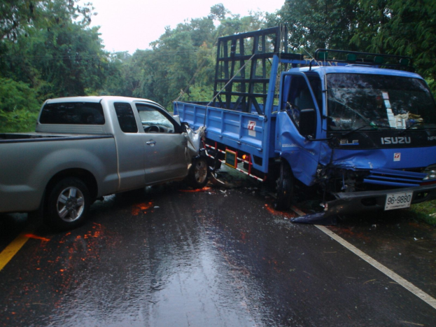 Ein schwerbeschädigter Lkw mit eingedellter Front und verbeulter Karosserie liegt auf der Seite an der Straße, umgeben von Bäumen unter einem klaren blauen Himmel.