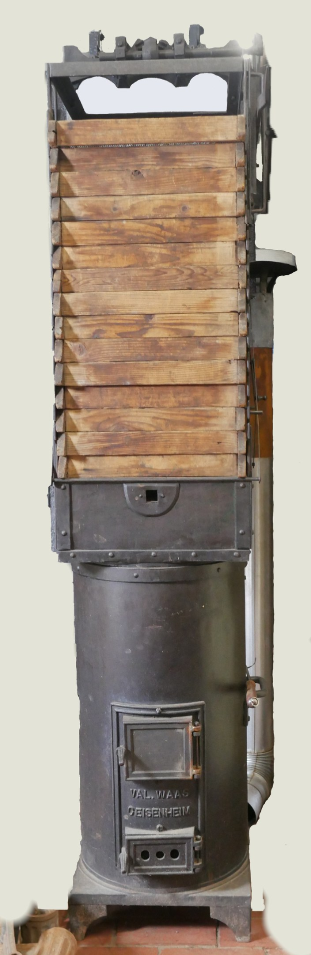 Alte Holzofen mit Metall- und Holzkonstruktion, Schornstein, auf einem Ziegelboden mit einer Wand im Hintergrund.