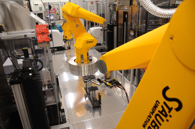 Gelber industrieller Roboter, der in einer Fabrikumgebung Maschinen bedient, mit sichtbaren Rohren, Equipment und Deckenbeleuchtung.