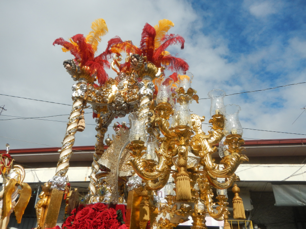 Ein großes goldenes und rotes Schwimmbad mit Blumen und anderen Dekorationsgegenständen bei einem Karnevalsumzug, mit einem Gebäude, Strommasten mit Drähten und einem bewölkten Himmel im Hintergrund.