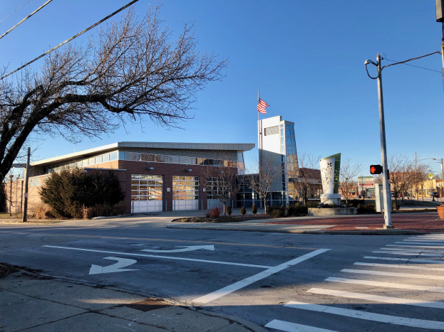 Großes modernes Feuerwachengebäude mit einer amerikanischen Flagge auf dem Dach, das an einer Straßenecke umgeben von Bäumen, Straßenlaternen und Versorgungsinfrastruktur liegt.