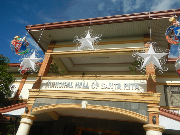 Municipal Hall of Santa Rita mit Fenstern, Säulen, einem Namensschild, dekorativen Dachschmuck, einem Baum auf der linken Seite und einem bewölkten Himmel als Hintergrund.