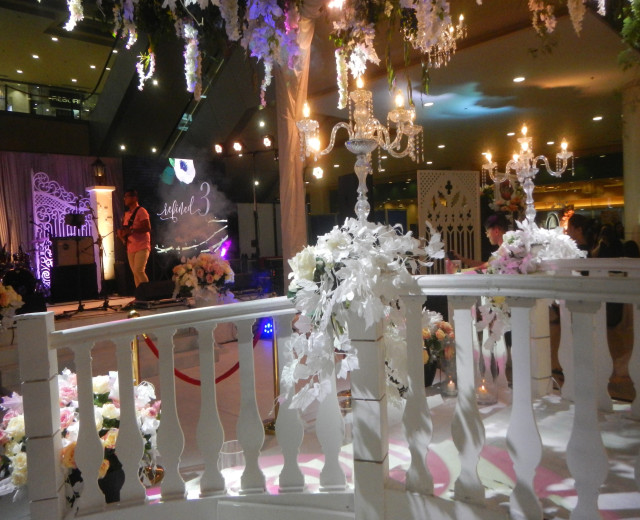 Eine Hochzeitszeremonie in einem großen Raum mit einem Kronleuchter, Blumenschmuck, Gästen, einem Redner, Musikinstrumenten, einem Schild und Dekolicht.