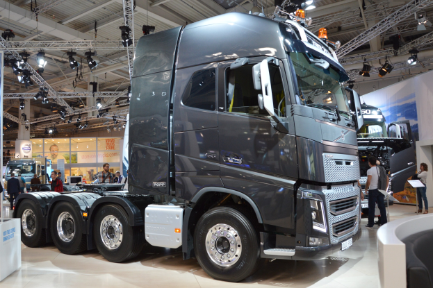 Großer Volvo FH16-Lkw auf einer Ausstellung präsentiert, umgeben von Besuchern, mit einer Couch, einem Tisch, Informationsplakaten und Deckenleuchten im Hintergrund.