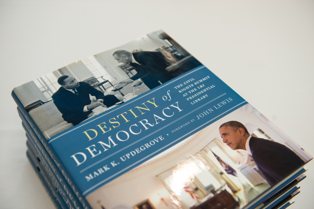 Ein Stapel Bücher mit dem Titel "Zukunft der Demokratie" mit Text und Bildern von Menschen auf den Umschlägen, auf einer weißen Oberfläche gestapelt.