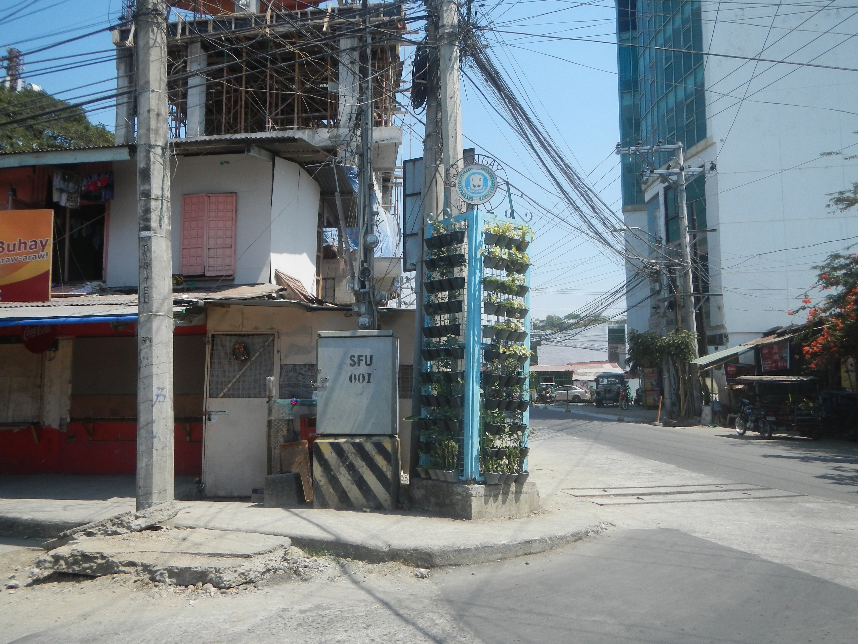Eine Stadtstraße mit Gebäuden, Strommasten, Kabeln, Schildern, Fahrzeugen, Bäumen und Himmel, mit einem Gebäude mit Drähten an der Seite im Vordergrund.