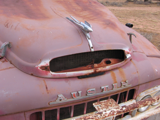 Alter rostiger Lkw auf einem Feld mit Bäumen und einem klaren blauen Himmel, der Spuren von langjähriger Witterungseinwirkung zeigt.