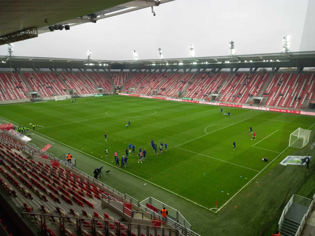 Ein Fussballfeld in einem Stadion mit Zuschauern drumherum unter Stadionbeleuchtung, mit dem Himmel im Hintergrund.