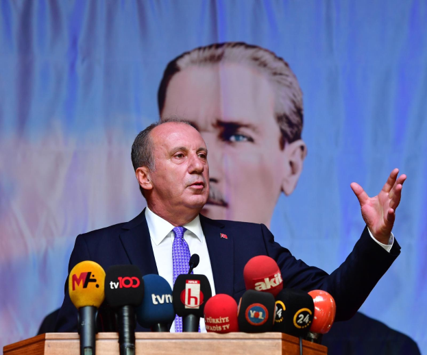 Ein Mann im Anzug und Krawatte steht an einem Podium mit Mikrofonen und spricht vor einem Bildschirm, wahrscheinlich zu der Ankündigung des Rücktritts des türkischen Präsidenten Recep Tayyip Erdogan.