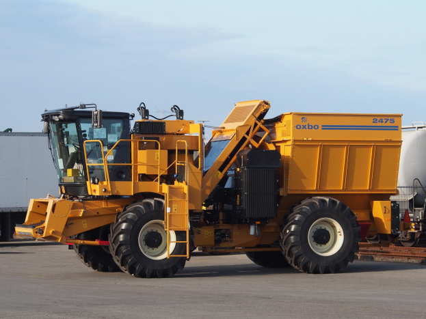 Großer gelber Volvo L220 Radlader vor einem weißen Container auf einer Straße mit einem klaren blauen Himmel geparkt.