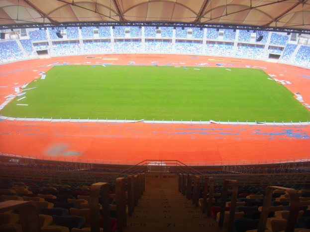 Ein großes Stadion mit vielen Zuschauern, das über Sitzreihen, Geländer, Treppen und ein Dach verfügt und den Spielplatz in der Mitte zeigt.