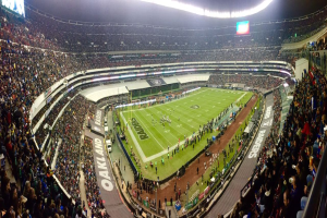 Ein großes Stadion voller Zuschauer, die ein Fußballspiel sehen, mit Spielern und verschiedenen Gegenständen auf dem Feld, beleuchtet von Deckenlampen, und mit Texttafeln, Geländern und Bildschirmen.