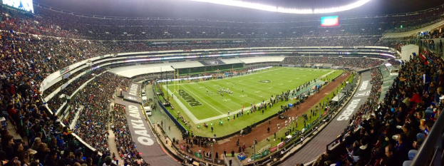 Ein großes Stadion voller Zuschauer, die ein Fußballspiel sehen, mit Spielern und verschiedenen Gegenständen auf dem Feld, beleuchtet von Deckenlampen, und mit Texttafeln, Geländern und Bildschirmen.