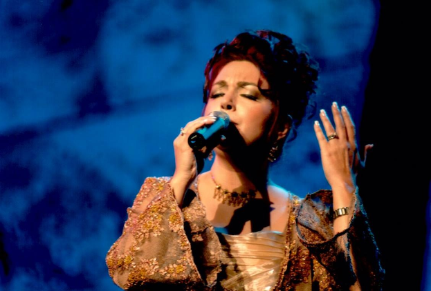 Frau in goldnem Kleid singend ins Mikrofon auf der Bühne der Eurovision Song Contest mit blauem und schwarzem Hintergrund.