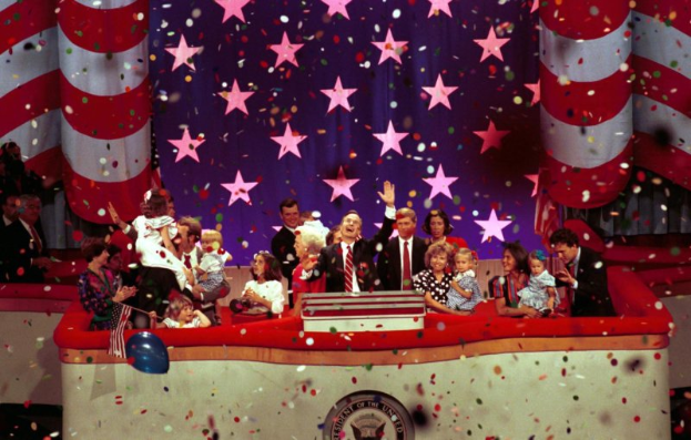 Eine Gruppe von Menschen steht auf einer Bühne mit einem Rednerpult, das ein Logo, Luftballons und Konfetti im Hintergrund zeigt.