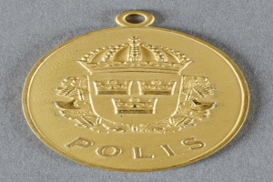 Goldene Medaille mit einer kronenförmigen Polizeimarke in der Mitte, mit eingravierter Schrift.