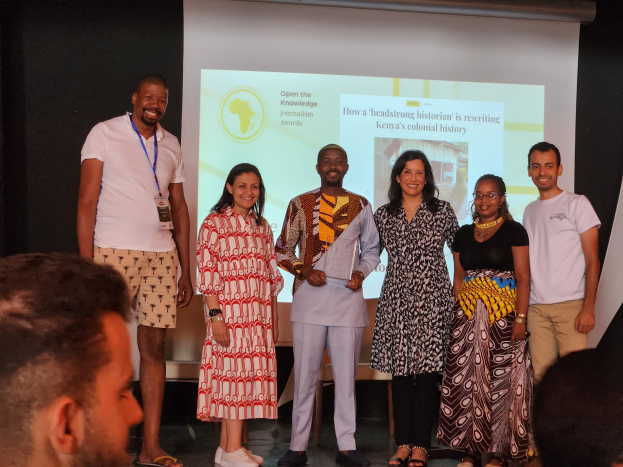 Eine Gruppe von Menschen auf einer Bühne, die lächeln und posieren, mit einem Publikum davor und einem Bildschirm im Hintergrund mit der Aufschrift "Open the Knowledge Journalism Awards 2019".