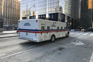 Rettungswagen auf einer städtischen Straße mit hohen Gebäuden, Straßenmöblierung und Passanten im Hintergrund.