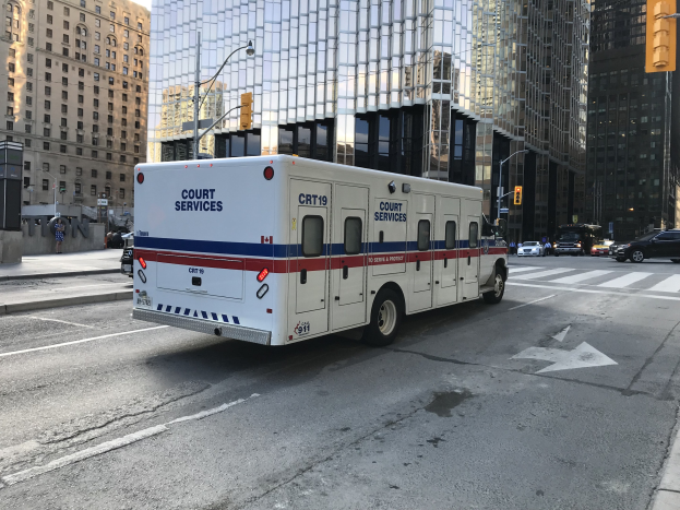 Rettungswagen auf einer städtischen Straße mit hohen Gebäuden, Straßenmöblierung und Passanten im Hintergrund.