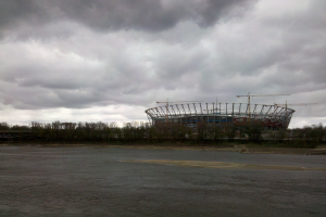 Das Olympiastadion in Kiew, Ukraine, ein großes Stadion umgeben von Bäumen und einer Brücke, mit einem bewölkten Himmel im Hintergrund und dem Boden unten.