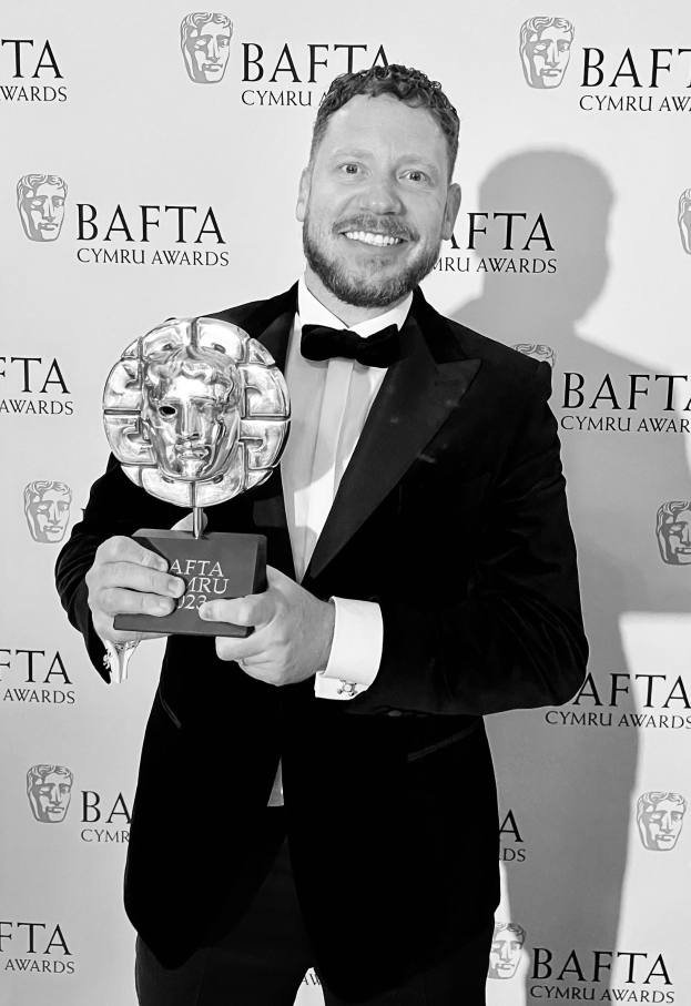 Ein Mann im Smoking, der eine BAFTA-Auszeichnung hält und lächelt, mit einem Hintergrund, auf dem 'BAFTA Awards 2018' steht