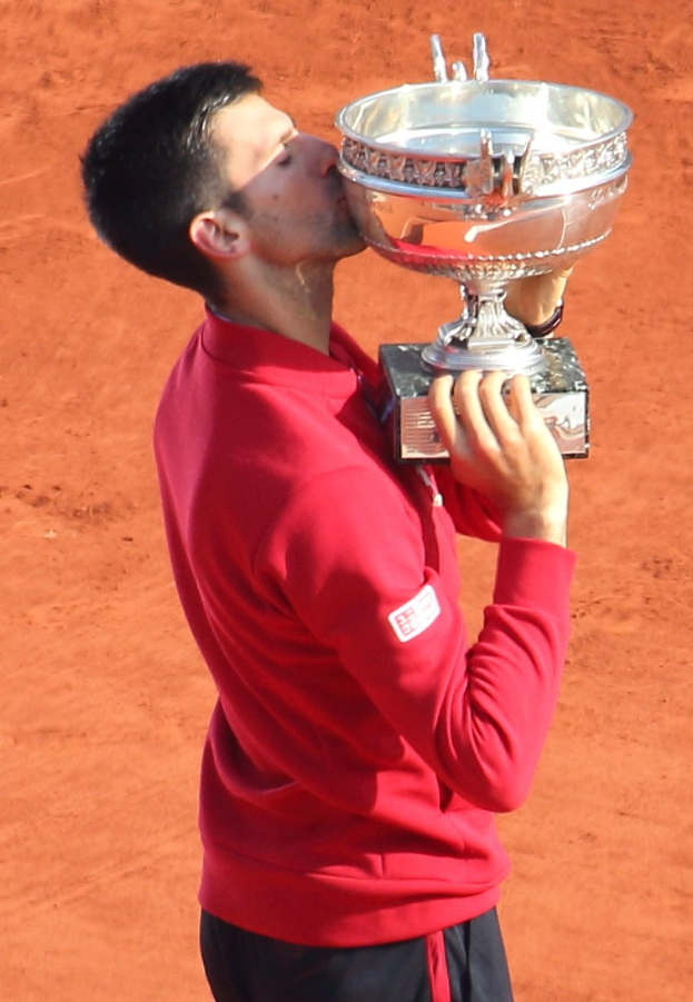 Novak Djokovic hält den French-Open-Pokal nach Sieg gegen Rafael Nadal im Finale der Herren-Einzel hoch und küsst ihn mit triumphierendem Gesichtsausdruck.
