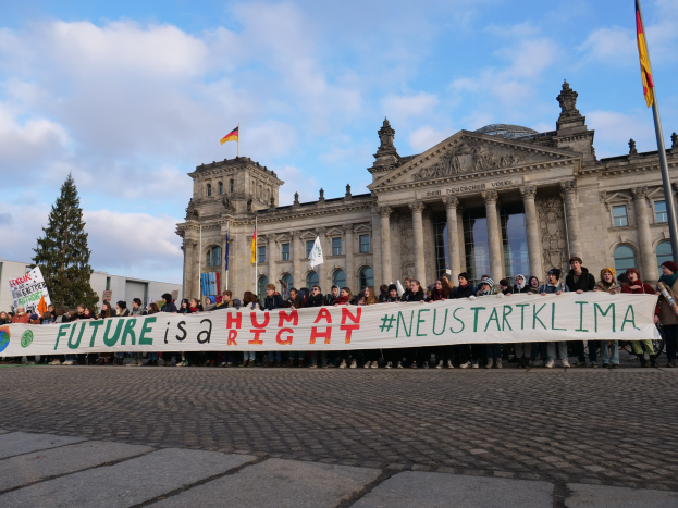 Gruppe von Menschen vor dem Reichstaggebäude in Berlin mit einem Banner, auf dem 'Zukunft ist ein Menschenrecht' steht