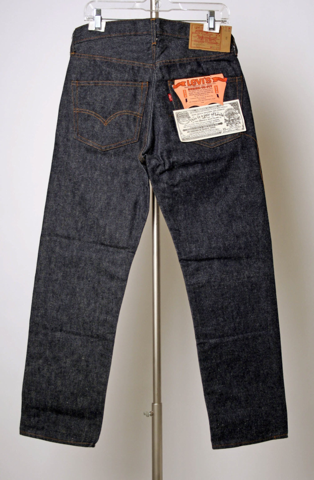 Klassische Levi's 501-Five-Pocket-Jeans mit Reißverschluss, Knopfverschluss und Levi's-Logo auf der Gesäßtasche, die an einem Metallständer an einer weißen Wand hängen.