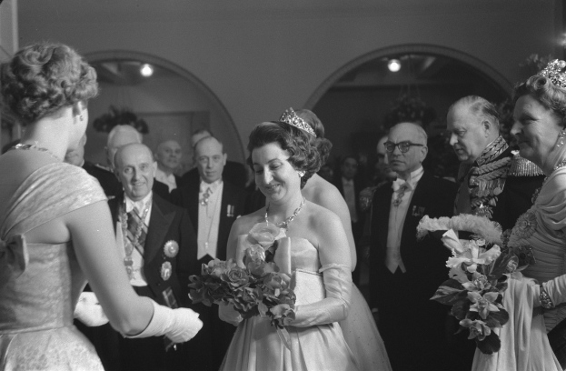 Schwarzes und weißes Foto von Queen Elizabeth II und Prinz Philip, Duke of Edinburgh, an ihrem Hochzeitstag, die Kronen tragen und Blumensträuße halten, umgeben von einer Gruppe von Menschen, mit Lichtern und einer Wand im Hintergrund.
