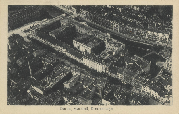 Ein altes Schwarz-Weiß-Foto einer Stadtlandschaft mit zahlreichen Gebäuden, darunter ein zentraler Wolkenkratzer, und Text am unteren Rand des Bildes.