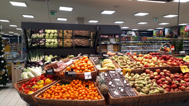 Ladeninneneinrichtung mit Körbüsen und Gemüsesel in Körbüsen, jeweils mit Preisschildern, einem beleuchteten Weihnachtsbaum links und Regalen mit anderen Artikeln im Hintergrund.