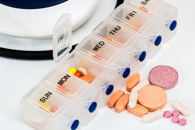 Weißer Tisch mit Pillendose, die Pillen enthält, und einem Stethoskop daneben, Pillendose mit Text beschriftet.