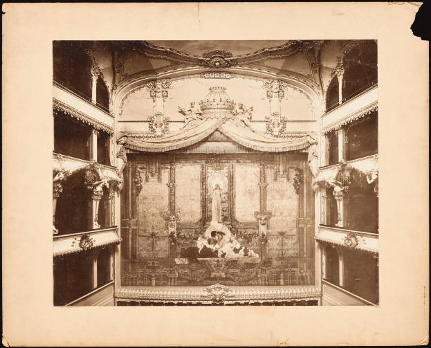 Ein altes Schwarz-Weiß-Foto eines Theaterinnenraums, mit ein paar Menschen auf der Bühne im Vordergrund und Skulpturen an den Wänden und der Decke.