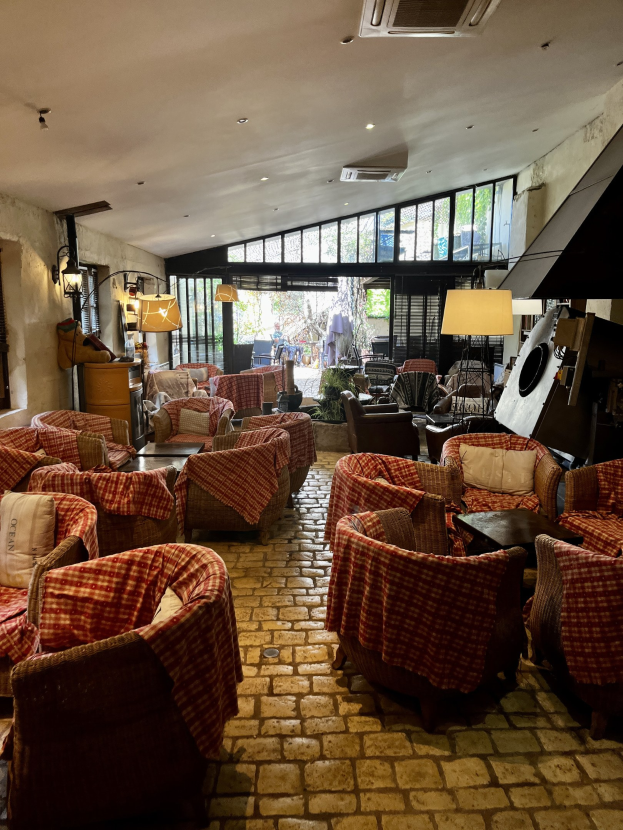 Großer Eingangsbereich des Rathauses de Ville mit zahlreichen Stühlen, Tischen, gepolsterten Sofas, wandmontierten Lampen, Deckenklimaanlage und Glasfenstern im Hintergrund.