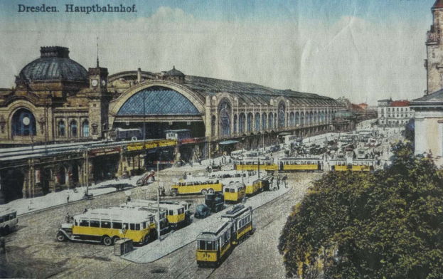 Schwarz-weiß-Postkarte des Dresdner Hauptbahnhofes in Deutschland, die eine belebte Straße mit Fahrzeugen, Fußgängern, Bäumen, Gebäuden und einem bewölkten Himmel zeigt.