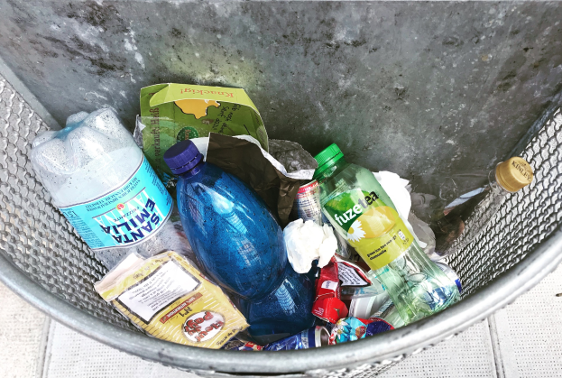 Ein Metallmülleimer voller verschiedener Plastikflaschen, Tüten und anderer Gegenstände.